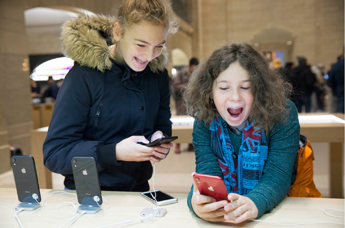 Two excited children playing with iPhones on display in an Apple store. 